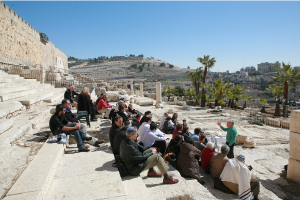 A group of people in Israel listening to a man teaching outside sitting on steps